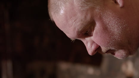 profile view on face of sweaty caucasian blacksmith forging iron in smithy