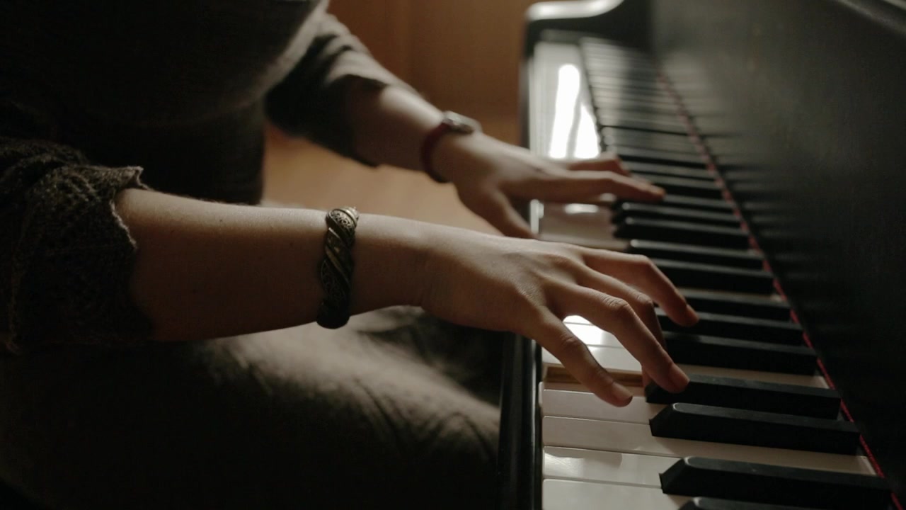 Cinematic close-up shot of a woman pianist playing music on a grand piano.