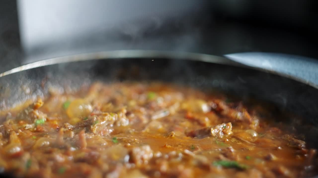 Close up view in slow motion of a Bubbly and hot beef with vegetables stew in a smoky pan.
