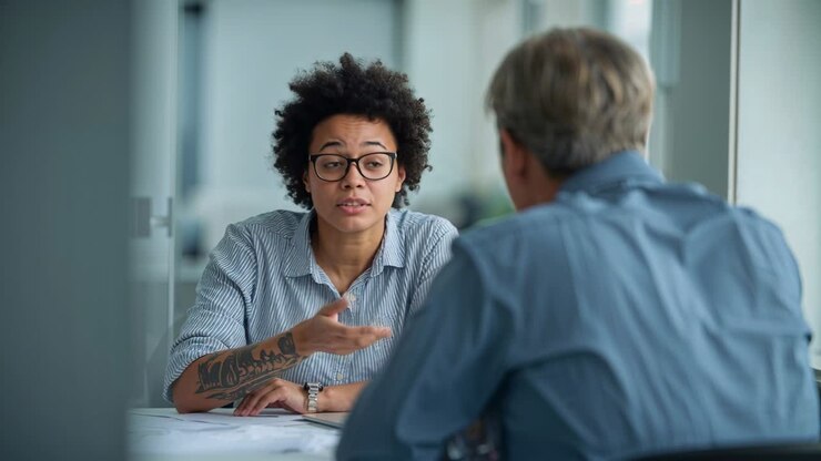 Explaining woman at meeting start in striped shirt raising hand at conference table showing papers