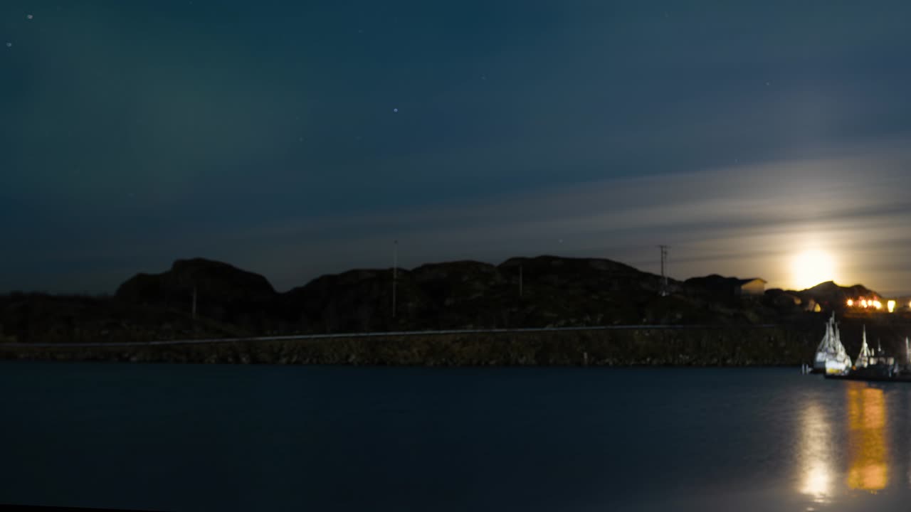 Alba lunare dietro nuvole leggere e deboli aurore boreali sulla baia. Time lapse 4K Norvegia. Toni di colore blu scuro, arancione e verde acqua