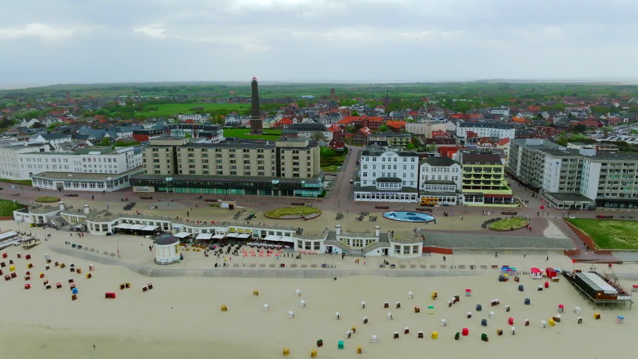 Pan right aerial view of Borkum island vast beach with strandkorb chairs and historical spa resorts and hotels along the town coastline