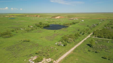 Ein-Blick-Auf-Ausgedehnte-Grüne-Felder,-Eine-Unbefestigte-Straße-Und-Einen-Teich-In-Der-Ländlichen-Gegend-Von-Kasachstan,-Zentralasien-–-Luftaufnahme-Einer-Drohne