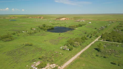 a view of expansive green fields, a dirt road, and a pond in the rural area of kazakhstan, central asia - aerial drone shot