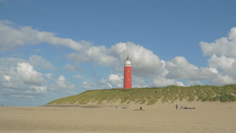 Steady-shot-of-the-Lighthouse-on-a-Dune-on-Texel-during-summer-on-a-half-sunny-day-with-passing-clouds,-Children-playing-and-running-on-the-beach