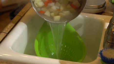 verter una olla de papas hervidas y zanahorias en un colador verde para drenar, cerrar