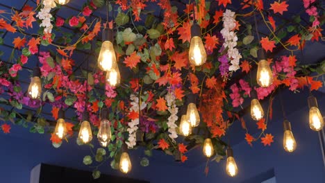 close up of string lights with artificial flowers and leaves hanging from ceiling