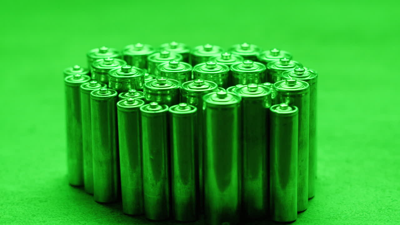 Silver batteries AA and AAA in neon light close-up. Double-A battery is a standard size single cell cylindrical dry battery. Batteries are common in portable electronic devices. An AA battery is composed of a single electrochemical cell that may be either a primary battery or a rechargeable battery.