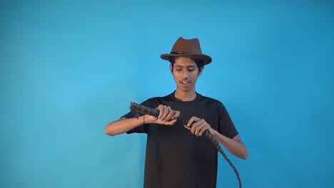 retrato de estudio de un joven sonriente confiado jugando con látigo en el fondo azul del estudio - filmado en cámara lenta