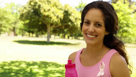 mujer feliz vistiendo rosa para concientizar sobre el cáncer de mama bebiendo agua
