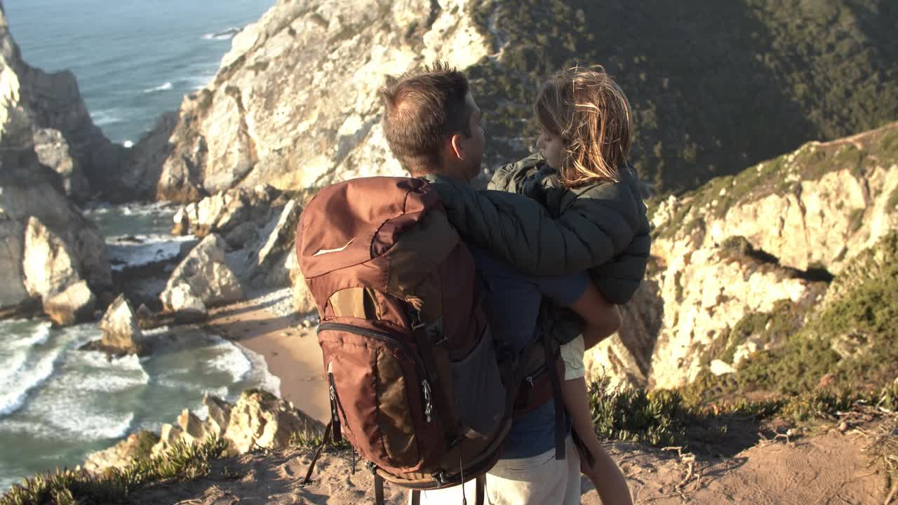 Padre con mochila de camping cargando a su hija en brazos