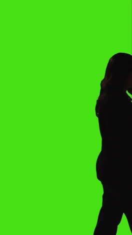 vertical video side view silhouetted shot of businesswoman talking on mobile phone walking across frame against green screen 2