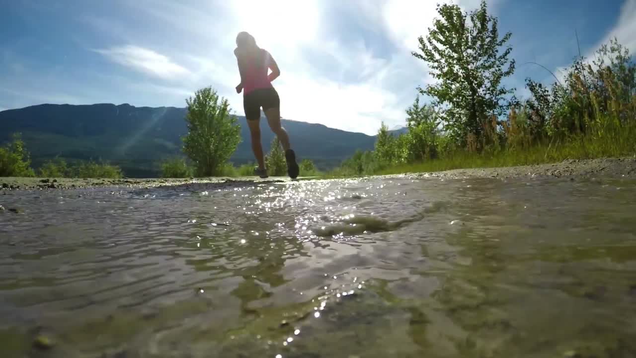 Rear view of fit woman jogging through puddle 4k