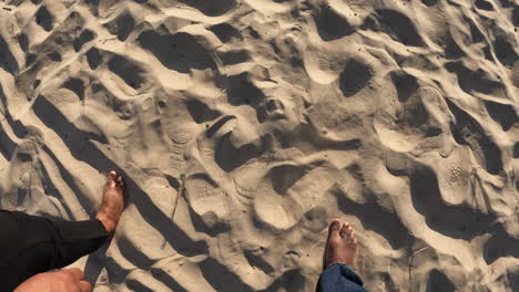 Looking-down-at-the-feet-of-a-black-couple-walking-along-a-sandy-beach-barefoot---point-of-view