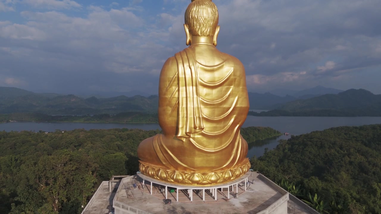 Primo piano aereo con drone di una scultura gigante dorata del Buddha che domina il paesaggio della Thailandia settentrionale.
