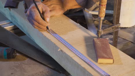 close-up carpenter measuring wood with a meter and taking notes.