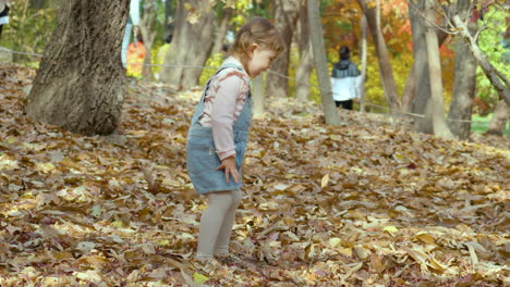 two year old asian girl throws leaves while playing in park