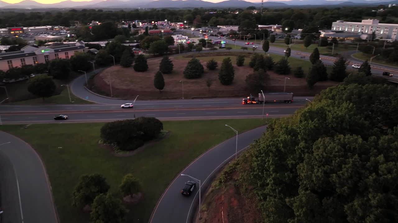 Aerial tracking shot of speeding police car with flashing lights on exit road of highway at dusk. American suburb town with oaring area in american town. Dusk scene. Police in action scene