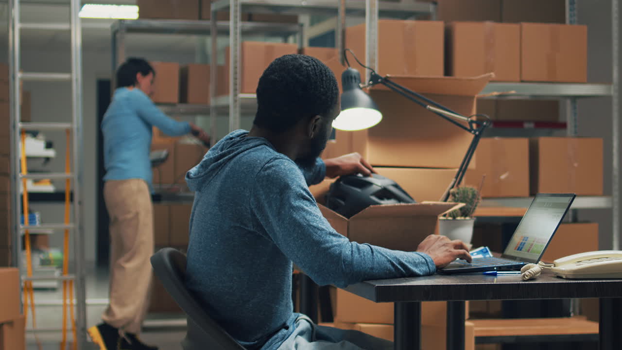 Man working on laptop in warehouse surrounded by boxes