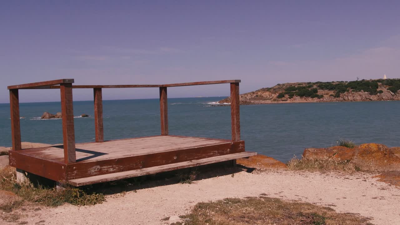 Uma plataforma de madeira se ergue à beira de um mar tranquilo, oferecendo uma vista serena da costa distante.