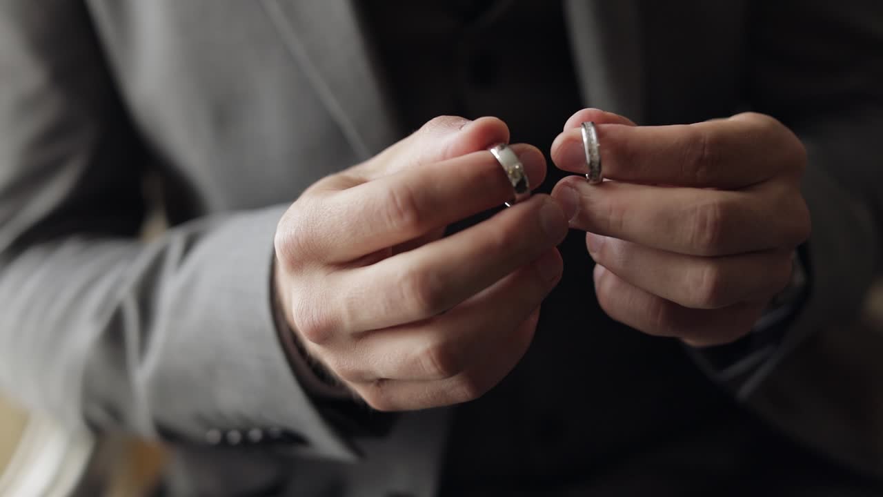 Groom in gray jacket holding wedding rings on palm of his hand, man touches the rings, slow motion