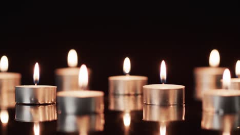 Video-of-rows-of-tea-candles-with-white-flames-and-copy-space-on-black-background