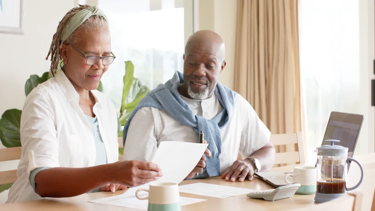 African american senior couple doing paperwork using laptop at home, slow motion