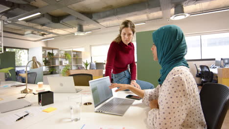 diverse female creative colleagues in discussion using laptop in office, slow motion
