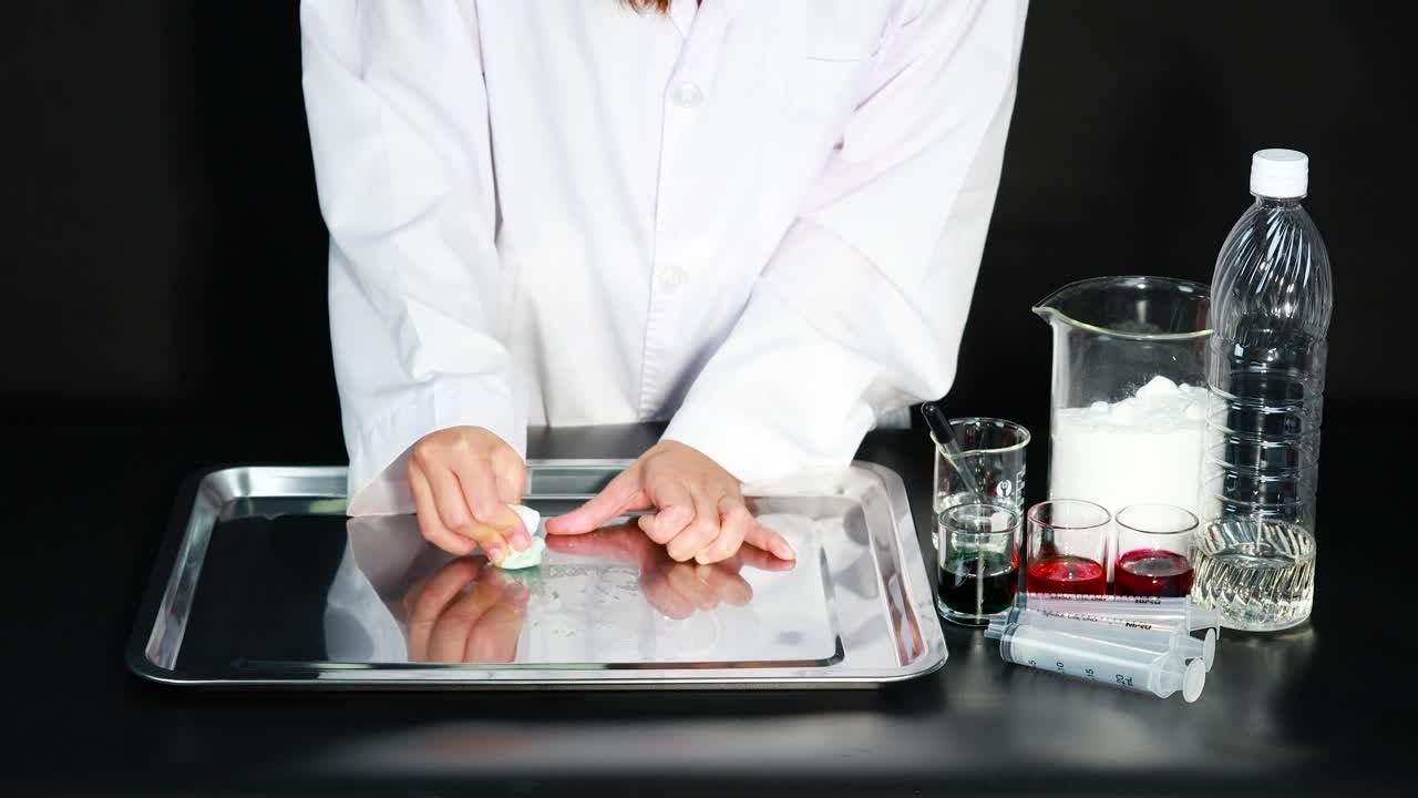 una persona con una bata de laboratorio demuestra la limpieza de una bandeja usando varios líquidos y materiales en un entorno controlado