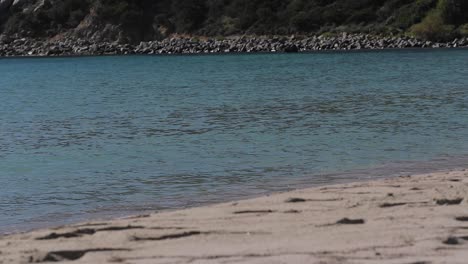 Toma-Estática-En-Cámara-Lenta-Para-Las-Olas-Del-Mar-En-Una-Playa-De-Arena-Y-Rocas-De-Montaña-En-El-Fondo