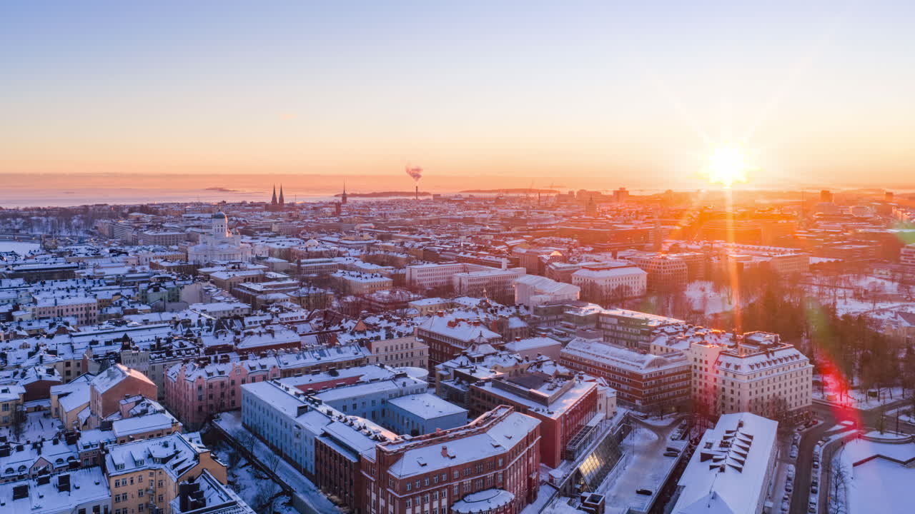Hyperlapse con drone, Kruununhaka, tramonto a Helsinki: sole basso che illumina i tetti innevati e la Cattedrale di Tuomiokirkko. Caldo bagliore dorato, skyline invernale. 4K UHD