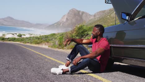 African-american-man-sitting-near-his-broken-down-car-on-road