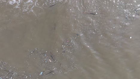 Drone-Giratorio-De-Arriba-Hacia-Abajo-De-Agua-Contaminada-Llena-De-Basura-Flotante-Y-Escorrentía-Fangosa-Del-Río-Mezclándose-Con-Agua-Tropical-Turquesa-De-Bali,-Indonesia