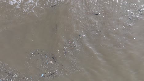 rotating top down drone shot of polluted water filled with floating trash and muddy river runoff mixing with turqouise tropical water of bali indonesia
