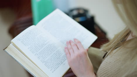 close up of chic white woman turning page, wearing necklace, seated on bench with blur view of shopping bag nearby in bright mall