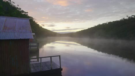 mist rising from a lake at sunrise in front of a boat shed