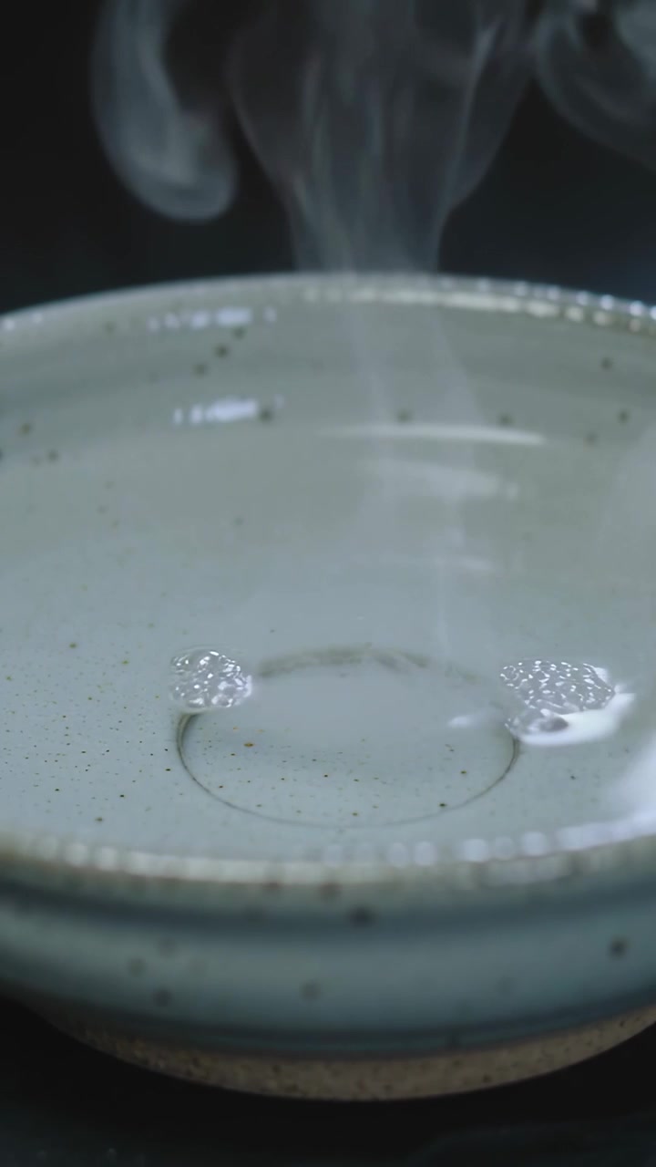Video verticale: Vapore che sale, ciotola smaltata che si riscalda dal basso su un tavolo scuro, con anello incassato