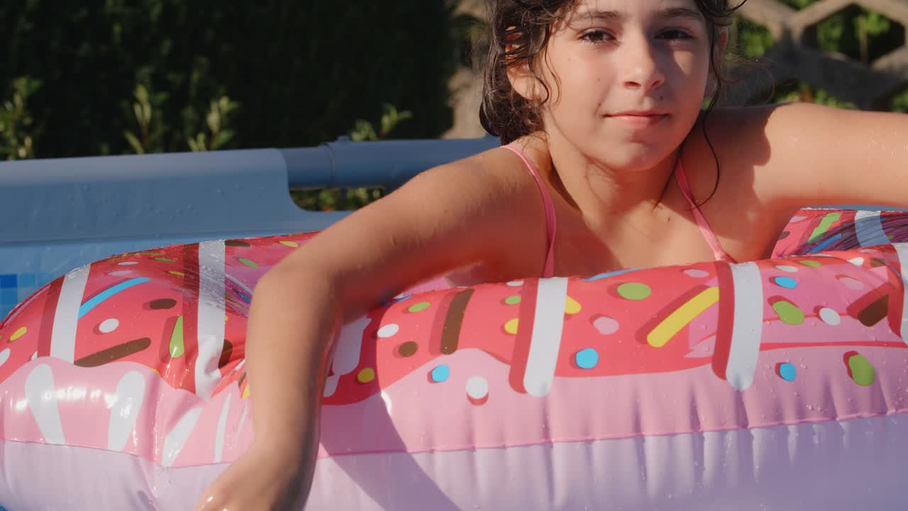 11-12 лет счастливая милая кавказская девушка лежит на надувном круге пончиков в бассейне в саду. прохладные летние каникулы для детей и детей. игры на воде. розовый donat. 4k замедленное движение