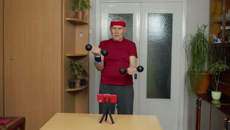 Senior-elderly-mature-man-watching-online-distance-workout-exercises-with-dumbbells-on-mobile-phone