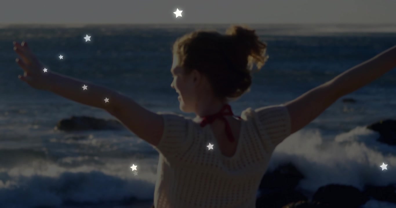 Mujer levantando los brazos en la orilla, activando superposiciones de estrellas flotando sobre las olas para un anuncio de entretenimiento.