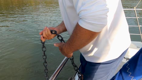 closeup of man letting down anchor chain with his hands on sailboat