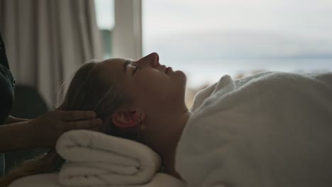 mujer joven recibiendo masaje de cabeza con impresionantes vistas al lago y la montaña