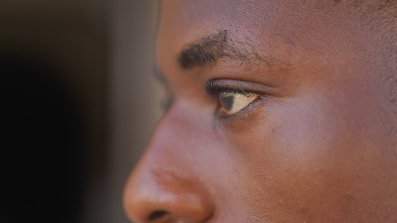 Closeup profile black athlete focusing, young sprinter locked in gaze, side portrait showing skin texture and eyebrow detail, quiet pregame concentration, cinematic shallow depth