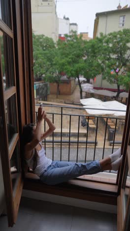 Woman relaxing on balcony, taking a photo of a rainy city scene