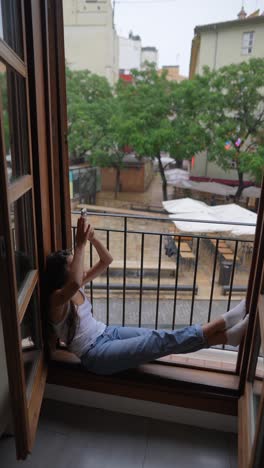 woman relaxing on balcony, taking a photo of a rainy city scene