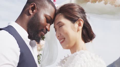 video of happy diverse bride and groom smiling and touching heads together at outdoor wedding