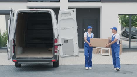 two young workers of removal company are loading boxes and furniture into a minibus