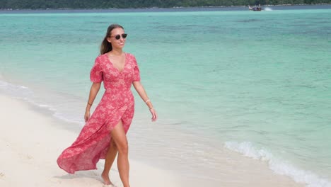 toma en cámara ultra lenta de una mujer caucásica bronceada con vestido rosa caminando por una hermosa playa en la isla de tailandia