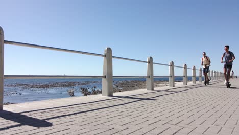 couple d'hommes gais heureux et diversifiés utilisant des scooters sur la promenade au bord de la mer, au ralenti