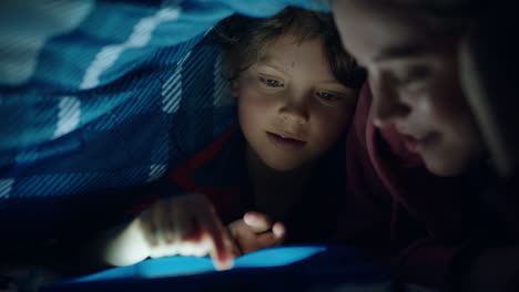 mother and child using tablet computer under blanket playing games on touchscreen technology little boy having fun before bedtime